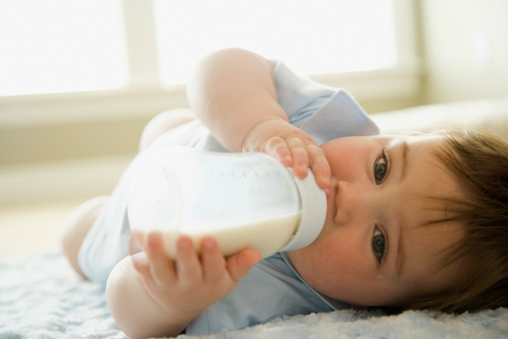 Un biberon bébé bien rempli de lait, que bébé boit allongé sur le lit.